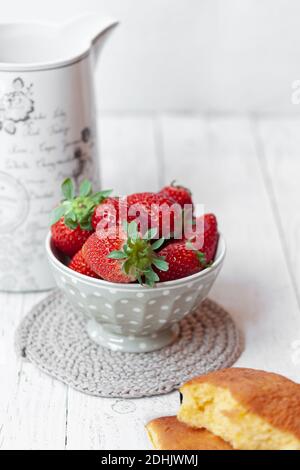 Traditionelle spanische süße sobao Kuchen in der Nähe Schüssel mit frischen platziert Reife Erdbeeren serviert zum leckeren Frühstück auf weißem Holztisch Stockfoto