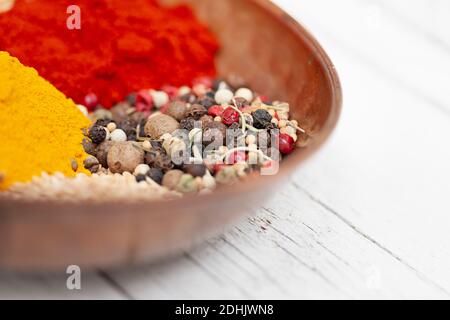 Nahaufnahme der Schüssel mit verschiedenen aromatischen bunten Gewürzen einschließlich Mischung Von Pfefferkörnern mit Paprika und Kurkuma-Pulver auf weiß gelegt Holztisch Stockfoto