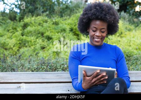 Inhalt Afrikanisch-amerikanische Freiberuflerin sitzt auf der Bank im Park Und mit Tablet arbeiten, während Remote auf Startup-Projekt Stockfoto