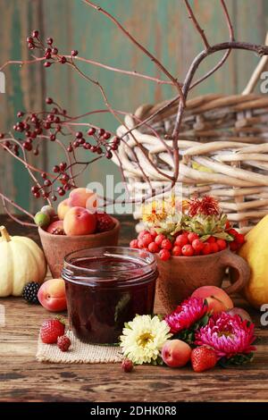 Dunkle Marmelade im Glasbehälter. Bunte Herbstfrüchte und Gemüse herum. Gesunde Ernährung Stockfoto