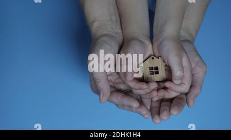 Die Hände der Mutter und des Vaters mit dem Kind halten die Figur in Form eines Hauses auf einem blauen Hintergrund. Stockfoto