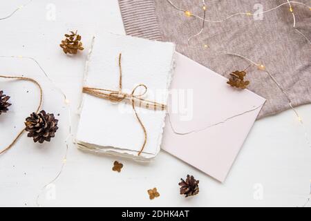 Kuschelige, flache Laie im Hygge-Stil. Weihnachtswunsch. Handgemachtes Papier mit Bastelfaden gebunden. Briefumschlag, Tannenzapfen, Bastelfaden und Kerze. Top Stockfoto