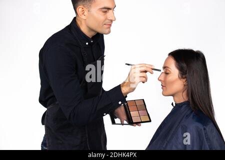 Geschlechterstereotypen. Männliche Make-up-Künstler macht eine Frau Make-up, hält eine kosmetische Palette auf einem weißen Hintergrund. Stockfoto