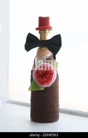 Hochzeitsflasche Champagner im Anzug des Bräutigams ist am Fenster auf der Fensterbank dekoriert. Hochzeitskomposition Stockfoto