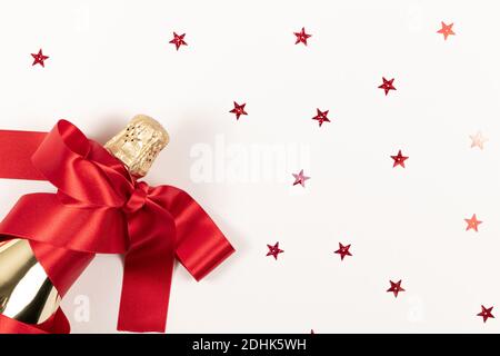 Eine Geschenkflasche Champagner in goldener Folie eingehüllt Ein rotes Seidenband und verstreute Konfetti auf einem weißen Hintergrund Stockfoto
