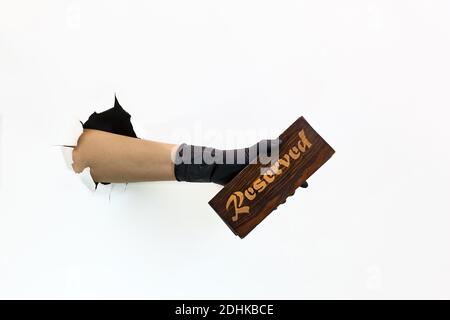 Eine weibliche Hand in einem schwarzen Latexhandschuh durch zerrissenes Papier auf weißem Hintergrund hält einen Holzteller zur Reserve. Quarantänemaßnahmen zur Verhinderung der SPRE Stockfoto