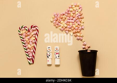 Gestreifte Lollipops in Herzform mit Marshmallows auf beigem Hintergrund. Schneemänner von Marshmallows und eine Tasse Kaffee. Weihnachtskonzept, Happy New Ye Stockfoto