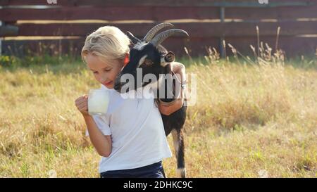 Ein Junge trinkt Ziegenmilch aus einem Becher neben seiner Ziege. Stockfoto