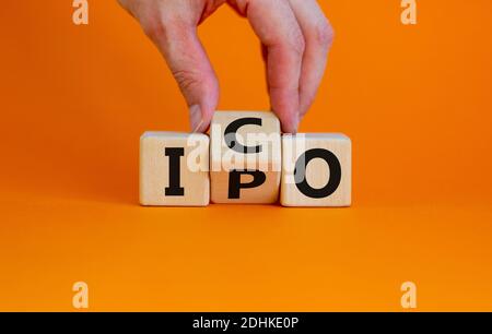 IPO vs. ICO. Hand dreht einen Würfel und ändert das Wort 'IPO - anfängliches öffentliches Angebot' in 'ICO - anfängliches Münzangebot'. Schöner gelber Tisch. Weiß, Bac Stockfoto