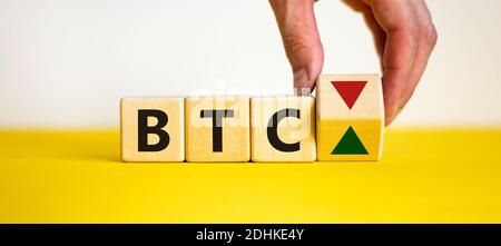 Hand dreht einen Würfel und ändert die Richtung eines Pfeils, der symbolisiert, dass der Wert der Kryptowährung Bitcoin nach oben oder unten geht. Wunderschön Stockfoto