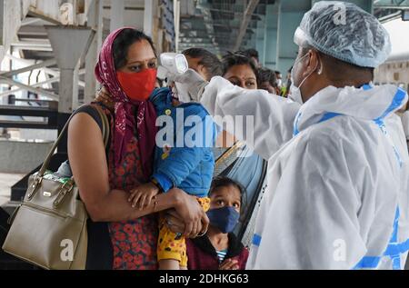 Mumbai, Indien. Dezember 2020. Gesundheitsfürsorge mit einem persönlichen Schutzanzug (PSA) Arbeiter überprüft die Temperatur einer Frau, die ein Kind während des Screenings trägt.Passagiere, die mit dem Zug aus dem Bundesstaat Kutch, Rajasthan und Madhya Pradesh reisen, werden untersucht und, wenn verdächtig gefunden, müssen Abstrichproben auf dem Bahngelände unterzogen werden. Kredit: SOPA Images Limited/Alamy Live Nachrichten Stockfoto