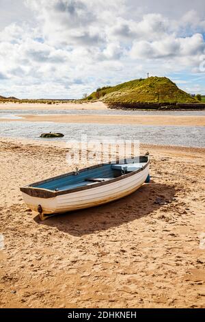 Ein kleines offenes Fischerboot am Strand bei Ebbe mit Church Hill im Hintergrund, in Alnmouth, Northumberland, Großbritannien Stockfoto