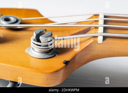 Detail eines Stimmpfostens auf dem hölzernen Kopfteil einer E-Bass-Gitarre. Musikinstrumente und Mechanik für Saitenstimmung. Stockfoto