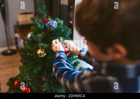 Familie weihnachtszeit zu Hause. Niedlichen kleinen Jungen Dekoration weihnachtsbaum drinnen während der Weihnachtszeit. Im Winter mit warmen natürlichen weichen Licht Stockfoto
