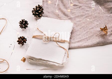Flach liegend im Hygge-Stil. Weihnachtswunsch. Handgemachtes Papier mit Bastelfaden gebunden. Briefumschlag, Tannenzapfen, Bastelfaden. Selektiver Fokus Stockfoto