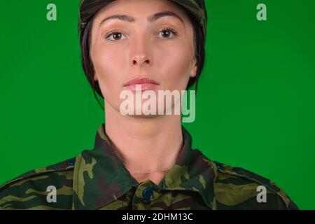 Porträt einer ernsthaften Frau in Militäruniform. Verletzung von Geschlechterstereotypen. Grüner Hintergrund. Stockfoto