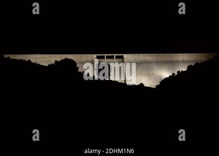 Enciso Damm beleuchtet in der Nacht mit einer Silhouette von Bergen und Eichen vor. Stockfoto