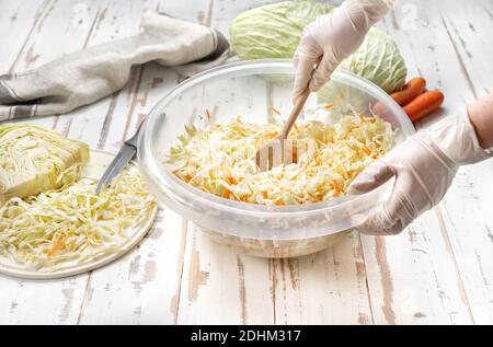 Weibliche Hände in Handschuhen Mischen gehackten Kohl in einer großen Schüssel. Sauerkraut. Fermentierte, probiotische und vegetarisch konservierte Nahrung Konzept für starke Immunit Stockfoto