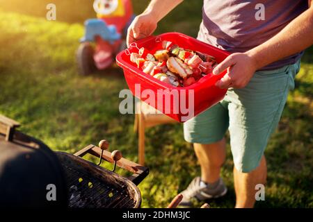 Verschiedene Arten von Fleisch und Gemüse werden in einem roten Kunststoffkorb bereit zum Grillen gebracht. Stockfoto