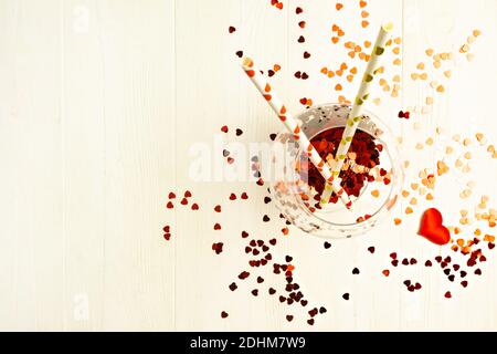 Glas mit herzförmiger Süßigkeit und einer Flasche Champagner auf hellem Hintergrund mit Platz für Text. Urlaubskonzept. Stockfoto