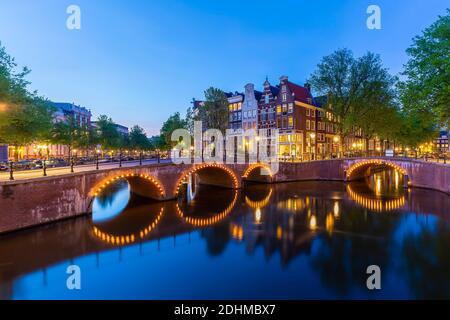 Amsterdamer Straßen und Kanäle in der Dämmerung. Brücken beleuchtet, Sommersaison. Beliebtes Reiseziel für Touristen. Stockfoto