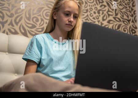 Teenager-Mädchen mit blonden Haaren arbeiten auf Laptop im Bett. Hohe Qualität Stockfoto