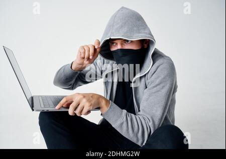 Ein Mann in einer Maske sitzt auf dem Boden innen Vor einem Laptop-Computer Hacking Verbrechen Stockfoto