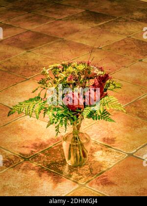Schöne Nahaufnahme Foto von getrockneten Herbst Bouquet mit wilden Blumen und grünen Pflanzen in durchsichtiger Glasvase auf rustikalen alten Fliesen Boden. Weiches Licht, b Stockfoto