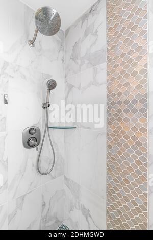 A custom tiled shower with marble and mosaic tiles and a chrome shower head. Stock Photo