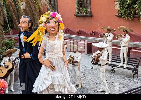 Eine traditionelle mexikanische Mariachi-Band spielt als riesige Puppen namens Mojigangas Tanz während einer Hochzeitsfeier im Lavaderos del Chorro Park in San Miguel de Allende, Guanajuato, Mexiko. Stockfoto