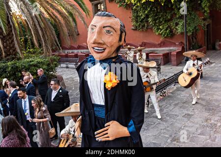 Eine traditionelle mexikanische Mariachi-Band spielt als riesige Puppen namens Mojigangas Tanz während einer Hochzeitsfeier im Lavaderos del Chorro Park in San Miguel de Allende, Guanajuato, Mexiko. Stockfoto