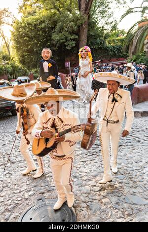 Eine traditionelle mexikanische Mariachi-Band spielt als riesige Puppen namens Mojigangas Tanz während einer Hochzeitsfeier Paraden durch die Straßen San Miguel de Allende, Guanajuato, Mexiko. Stockfoto