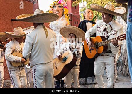 Eine traditionelle mexikanische Mariachi-Band spielt als riesige Puppen namens Mojigangas Tanz während einer Hochzeitsfeier Paraden durch die Straßen San Miguel de Allende, Guanajuato, Mexiko. Stockfoto