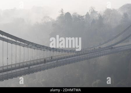 Radfahrer und Fußgänger überqueren die berühmte Clifton Suspension Bridge an einem nebligen Morgen in Bristol. Stockfoto