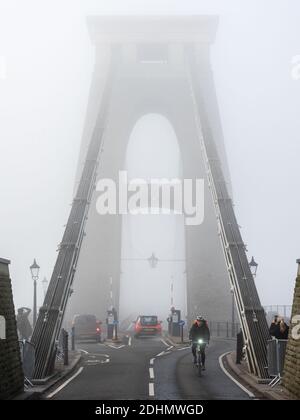 Ein Radfahrer überquert die markante Clifton Suspension Bridge, die im Herbst in Bristol von Nebel umhüllt ist. Stockfoto