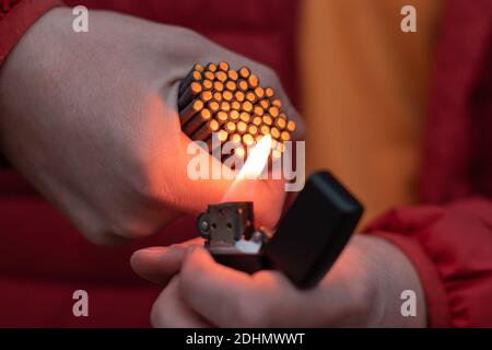 Man in Red Jacked Beleuchtung bis viele kleine schwarze Feuerwerkskörper in der Hand mit Benzin Feuerzeug. Guy Getting Ready for New Year Spaß mit Feuerwerk oder P Stockfoto