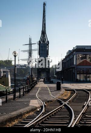 Fußgänger und Jogger passieren an einem Sommermorgen an Bristol's Harbourside alte Hafenkräne vor dem M Shed Museum. Stockfoto