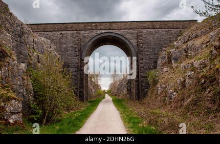 Der Tissington Trail, eine ehemalige Bahnstrecke, die durch einen Felsschnitt und unter einer hohen Steinbogenbrücke im Derbyshire Peak District verläuft Stockfoto