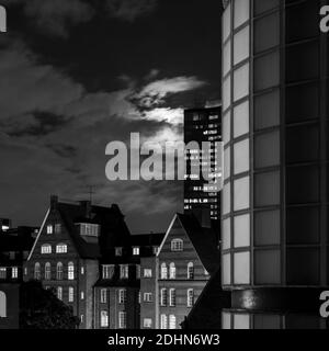 Schwarz-weiß monochrome, unbunter Blick auf die mondbeleuchteten Wolken Altes, rotgemauertes Gebäude in der Nacht mit modernen Gebäuden im Hintergrund Stockfoto