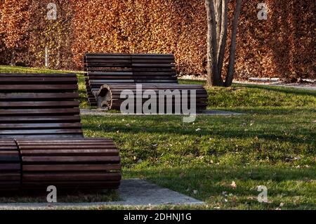 Moderne Holzbank im Herbstpark. Chill-Bereich in der Nähe des Stadions. Stockfoto