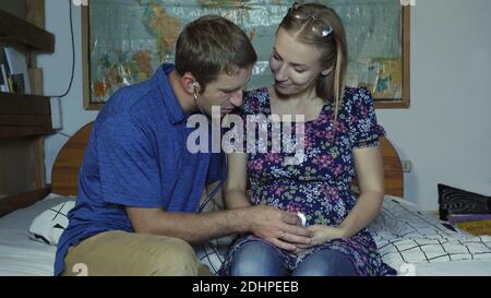 Ein liebevoller Ehemann hört auf den Bauch einer schwangeren Frau mit Stethoskop. Stockfoto