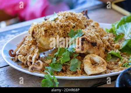 Gebratener Tintenfisch mit galic und Koriander oben in weißer Schale auf Holztisch, fertig zum Essen. Stockfoto