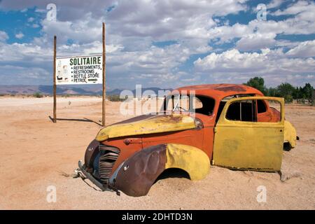 Ein rostiger Wagen sitzt im Sand an der Solitaire Tankstelle, dem Restaurant und dem General Store auf der Straße zu den Dünen bei Sossusvlei in Namibia. Stockfoto