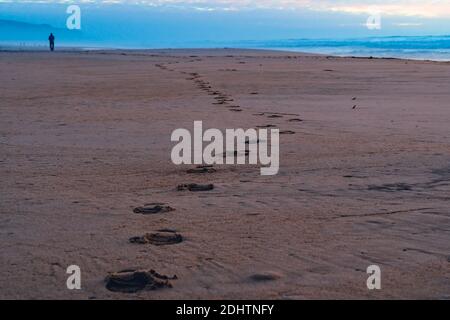 Abstrakte Landschaft, Sonnenuntergang am Strand und Schritte im goldenen Sand mit bewölktem Himmel auf dem Hintergrund Stockfoto