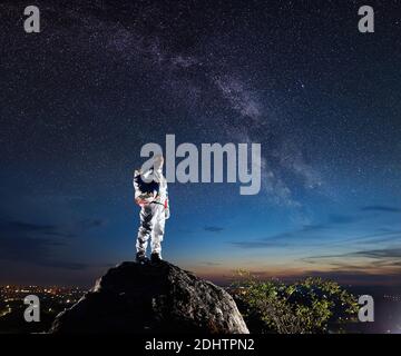 Seitenansicht des Weltraumreisenden, der auf einem felsigen Hügel steht und auf einen wunderschönen Sternenhimmel blickt. Astronaut im weißen Raumanzug mit Helm. Konzept der Raumfahrt und Milchstraße. Stockfoto