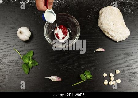 Mädchen Koch gießt Sahne in Tomatenmark für die Herstellung frisch italienische hausgemachte Pizza Stockfoto