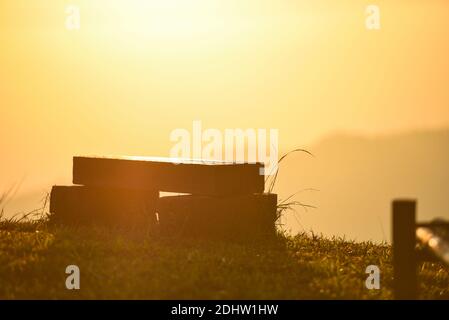 Natur warmes Licht mit Holzbank auf Graswiese mit sonnenaufgang oder Sonnenuntergang im Hintergrund der Berge Stockfoto