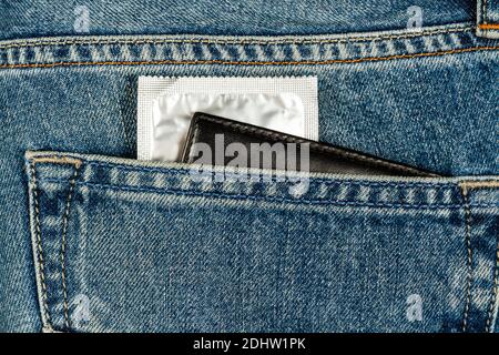 Ein Kondom in einer silbernen Packung und eine Brieftasche kleben Aus einer Jeans-Tasche Stockfoto