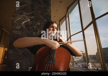 Teenager-Mädchen mit Cello, posiert in einem Flur. Stockfoto
