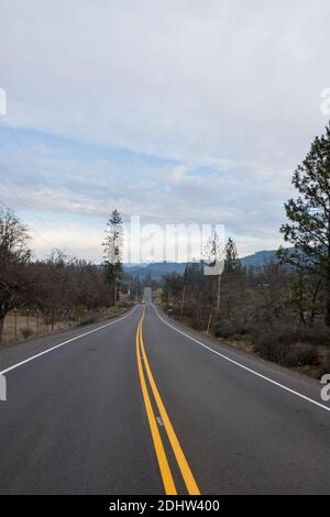 Leere Straße mitten in der trockenen Natur mit Bergen In der Ferne Stockfoto